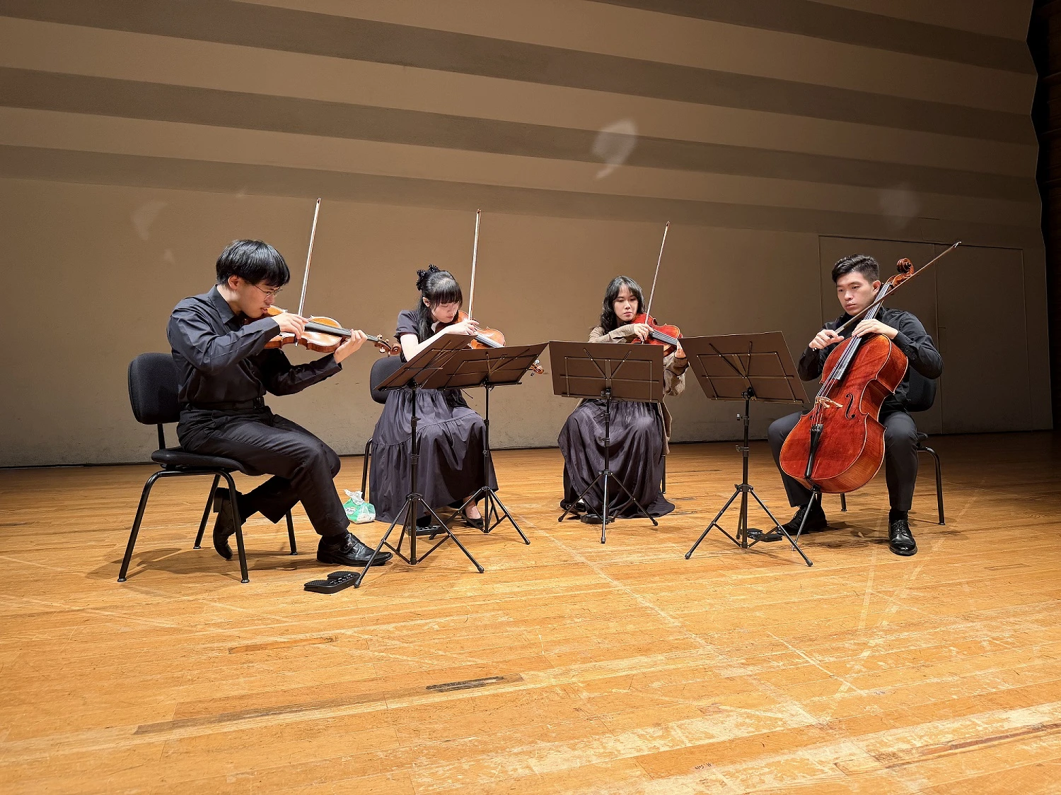 四位青年音樂家坐在舞台上演奏樂器,包含小提琴、中提琴和大提琴。