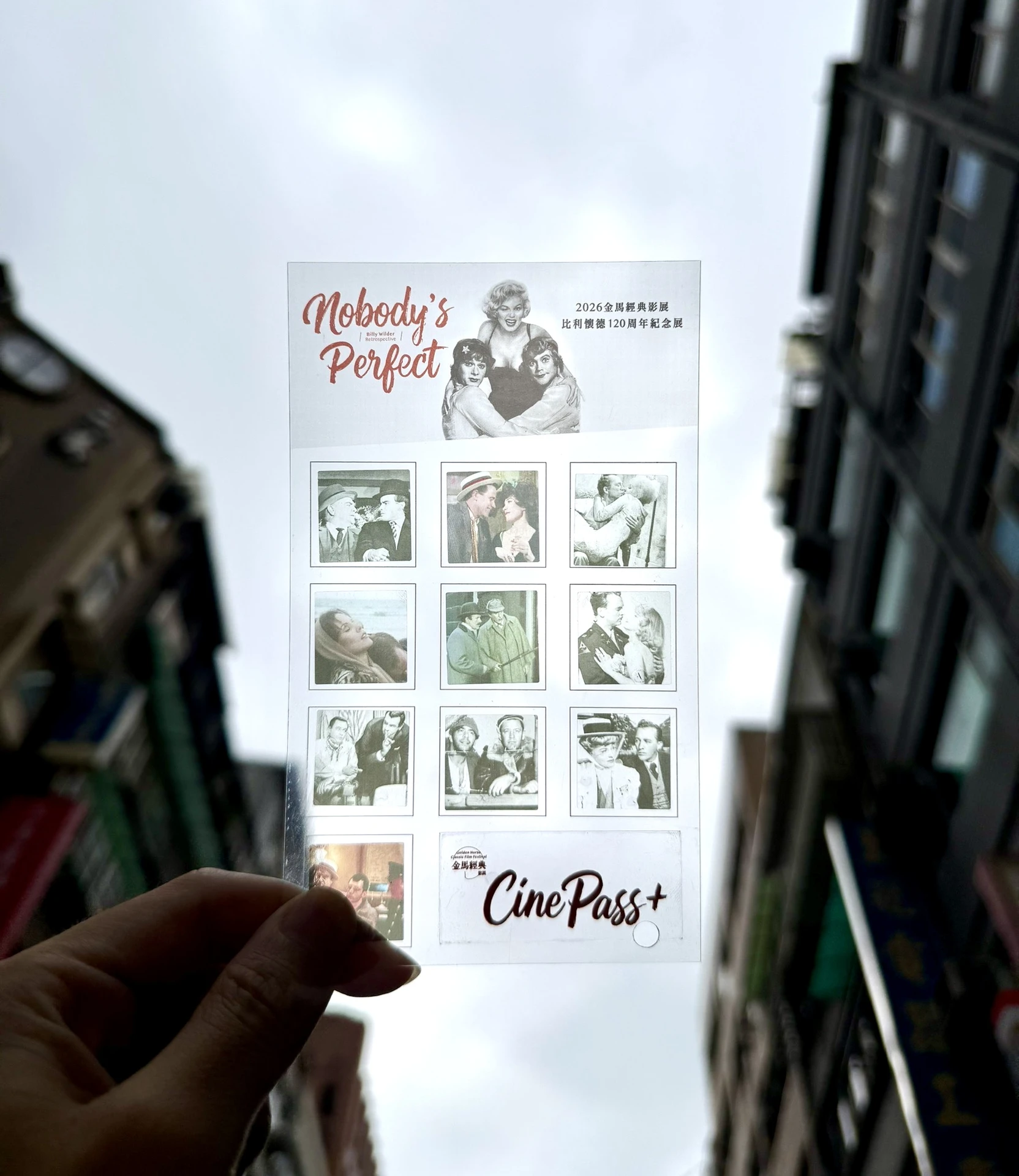 一隻手將印有「Nobody's Perfect」及12空格集點格子的「CinePass+」透明集點卡舉高，透出背後的建築物與天空。
