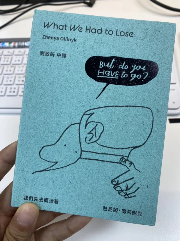 一隻手拿著淺藍綠色外觀的小書《我們失去而活著》，書封上有簡單的手繪線條與英文字。