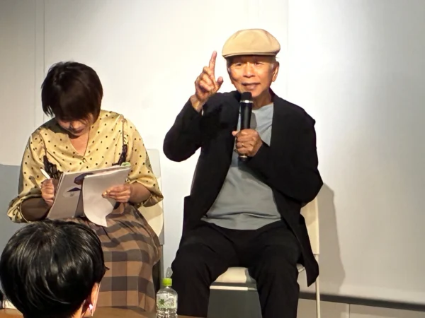 攝影家阮義忠戴帽在台上拿麥克風發言，比出手指手勢