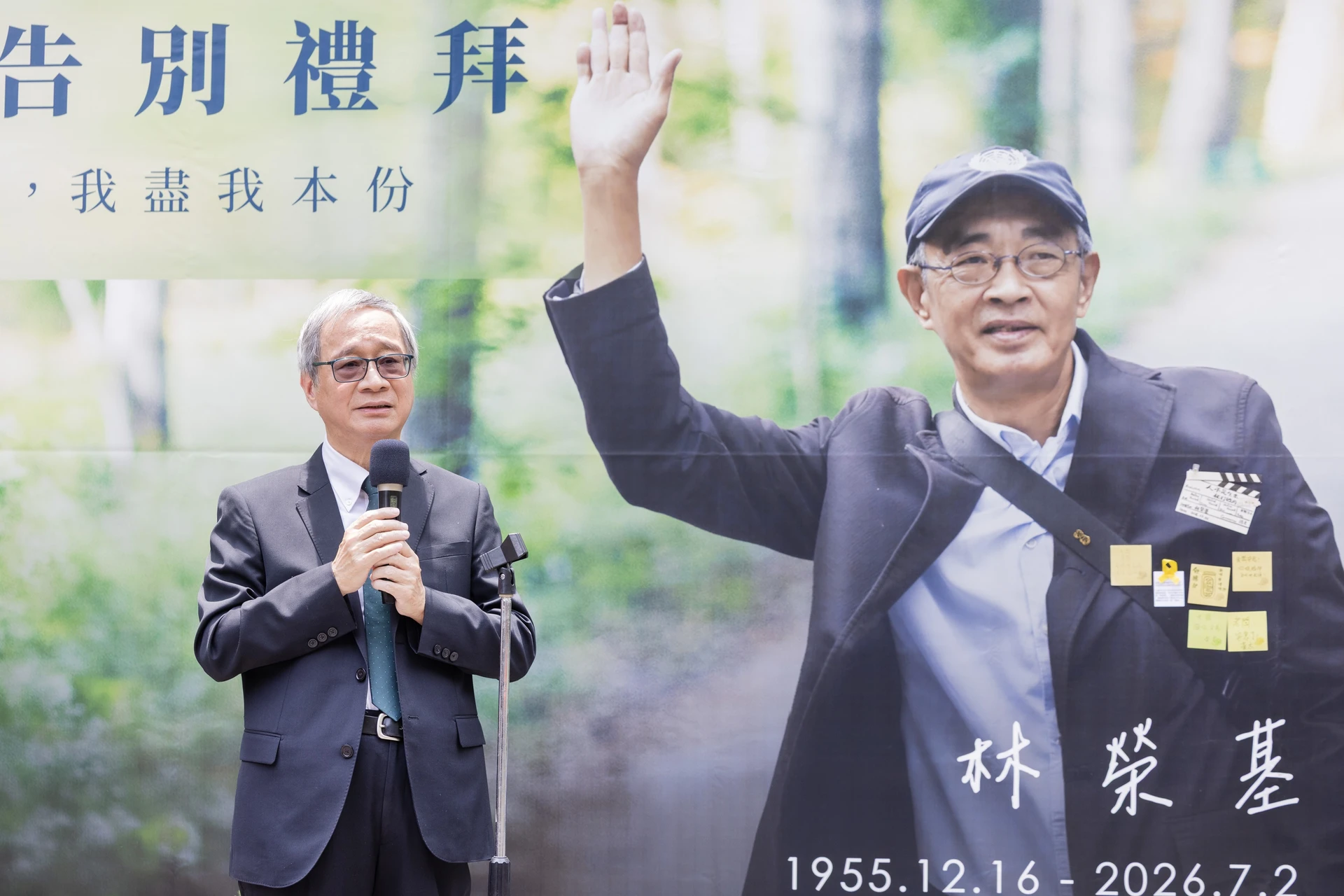 文化部長李遠身穿西裝、打領帶,手持麥克風在講臺前發言,背景為林榮基舉手揮別的巨大海報與生卒年。