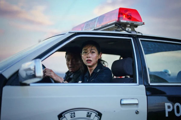 女星鄭好娟坐在警車駕駛座上神情緊張，車頂裝有紅色警示燈，副駕駛座可見黃晸珉。