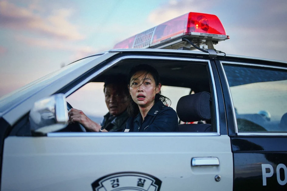 女星鄭好娟坐在警車駕駛座上神情緊張，車頂裝有紅色警示燈，副駕駛座可見黃晸珉。