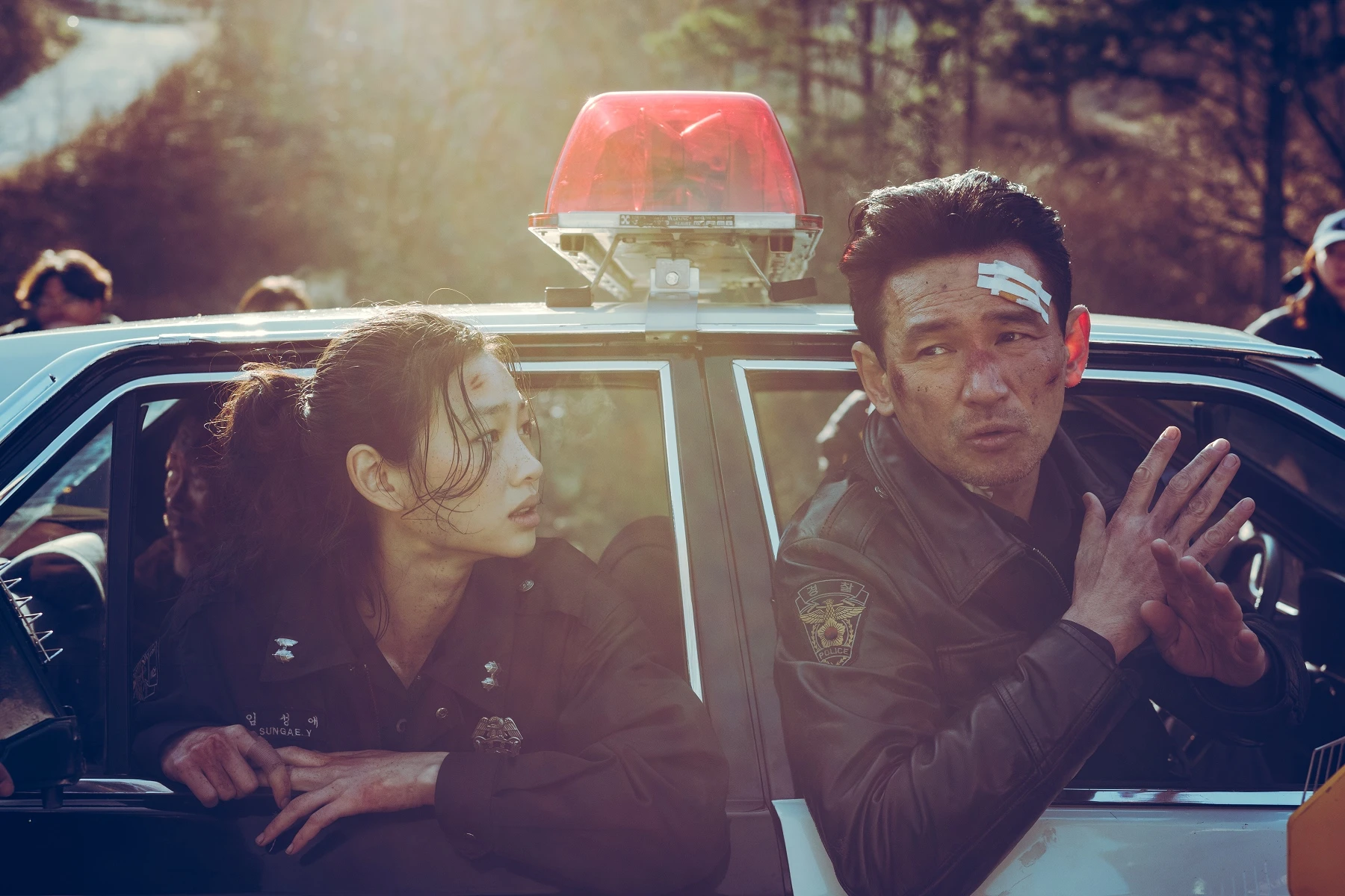 鄭好娟與黃晸珉坐在警車內，黃晸珉額頭貼著紗布並比出手勢，兩人正在對戲。