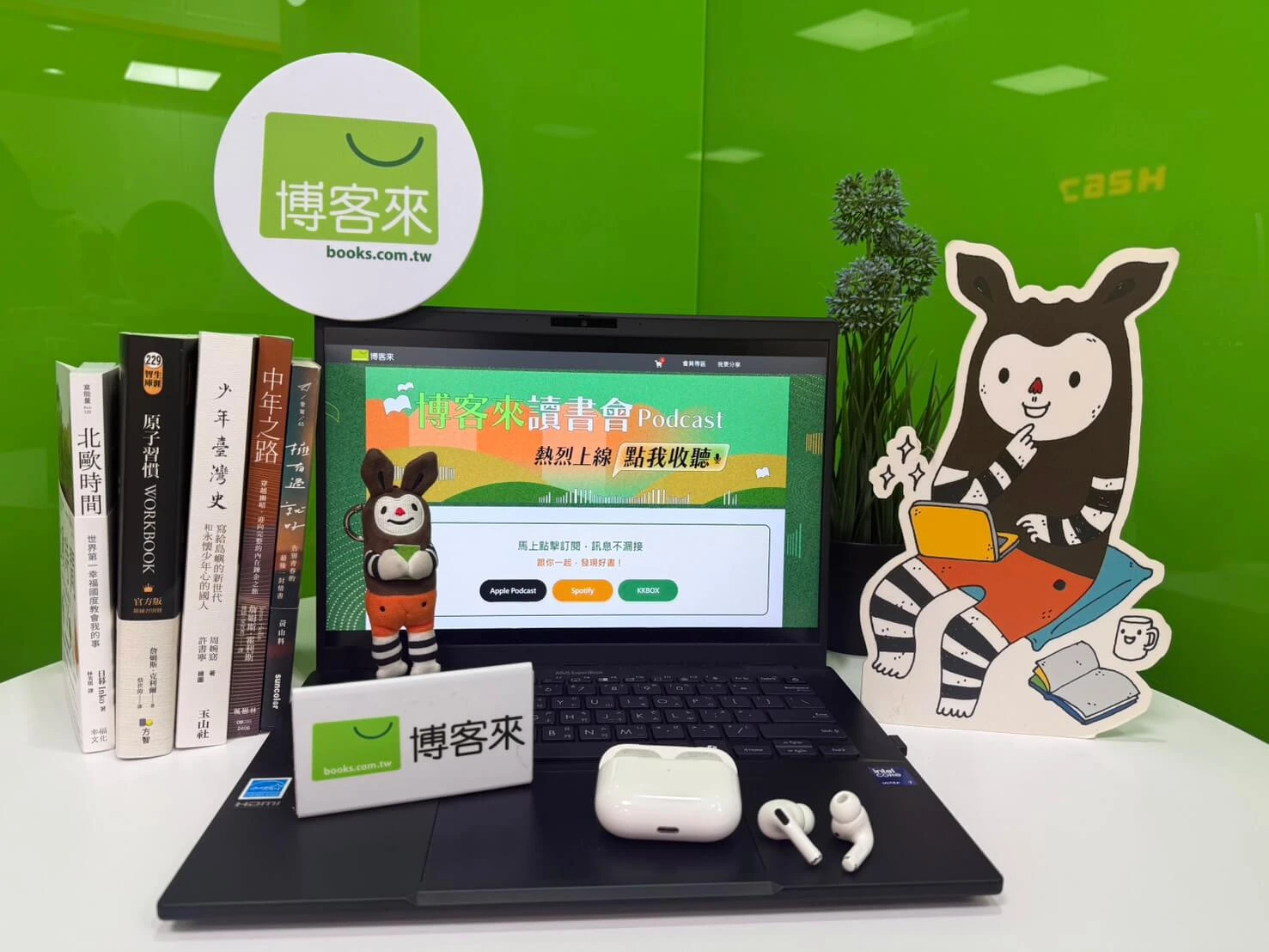 筆記型電腦螢幕顯示《博客來讀書會》Podcast畫面,周圍擺放多本書籍與吉祥物立牌。
