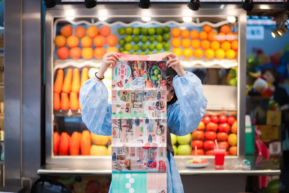 一名女子手持誠品生活南西《風格冰菓室》中英雙語觀光地圖，背景為色彩繽紛的水果攤。