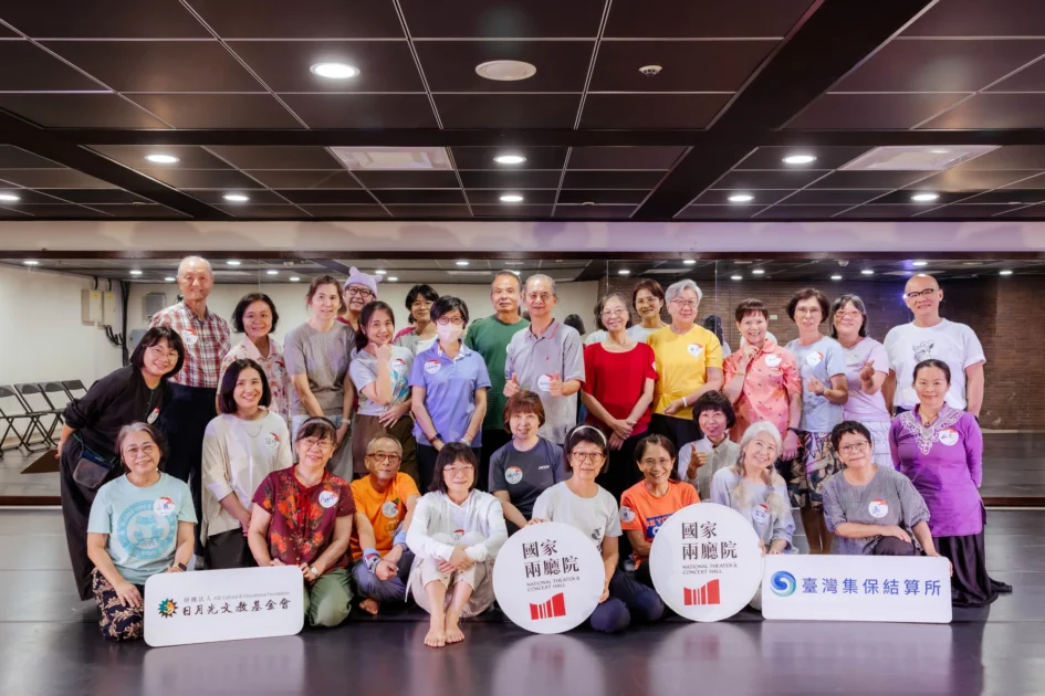 多位熟齡學員與工作人員在排練室內合影，部分學員手中拿著寫有「國家兩廳院」、「日月光文教基金會」、「臺灣集保結算所」字樣的標示牌。