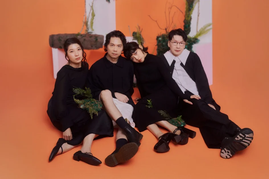 四位男女音樂人與演員坐在橘色背景前合影，其中一女將頭輕靠在身旁男性肩上，服裝皆以黑色系為主。