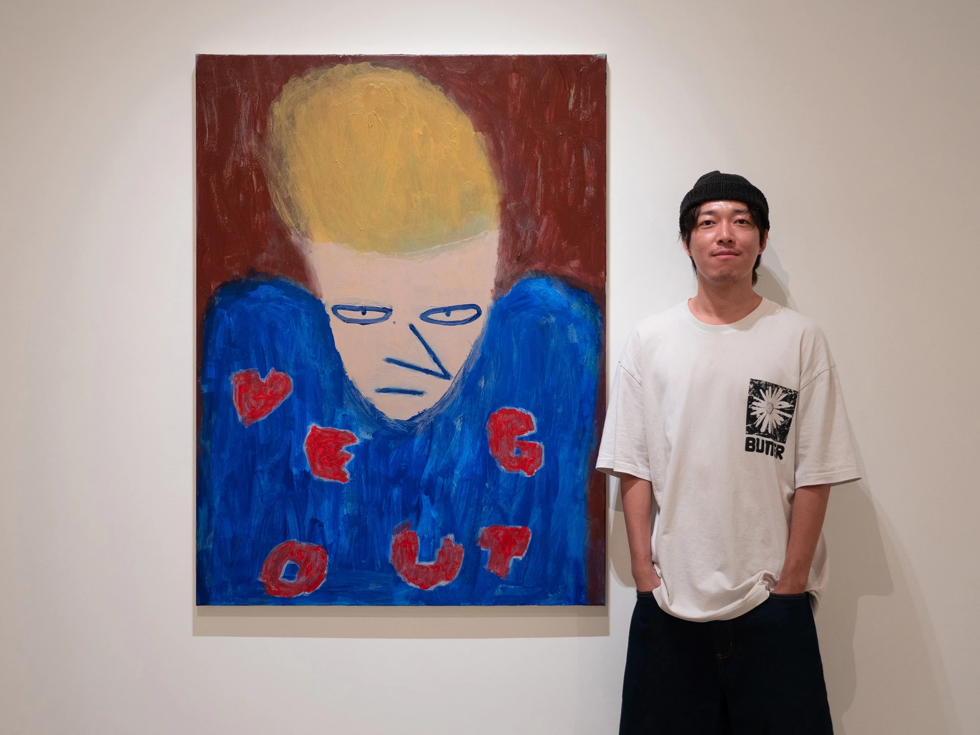 藝術家桑拿大可站在他的藍色調自畫像畫作旁,畫中人物留著黃髮並帶有招牌的慵懶厭世神情。