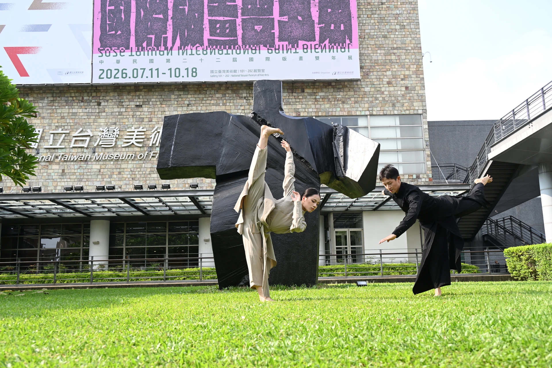 兩位舞者在戶外雕塑園區朱銘作品前進行現代舞表演,姿勢優美且充滿動感。
