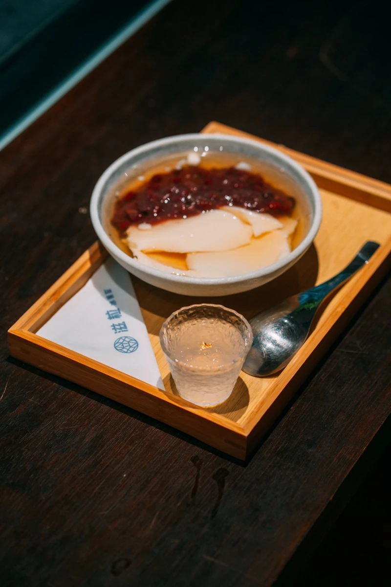 木製托盤上擺放著一碗裝有紅豆與豆花的瓷碗，以及一杯點綴金箔的透明燕窩飲品。