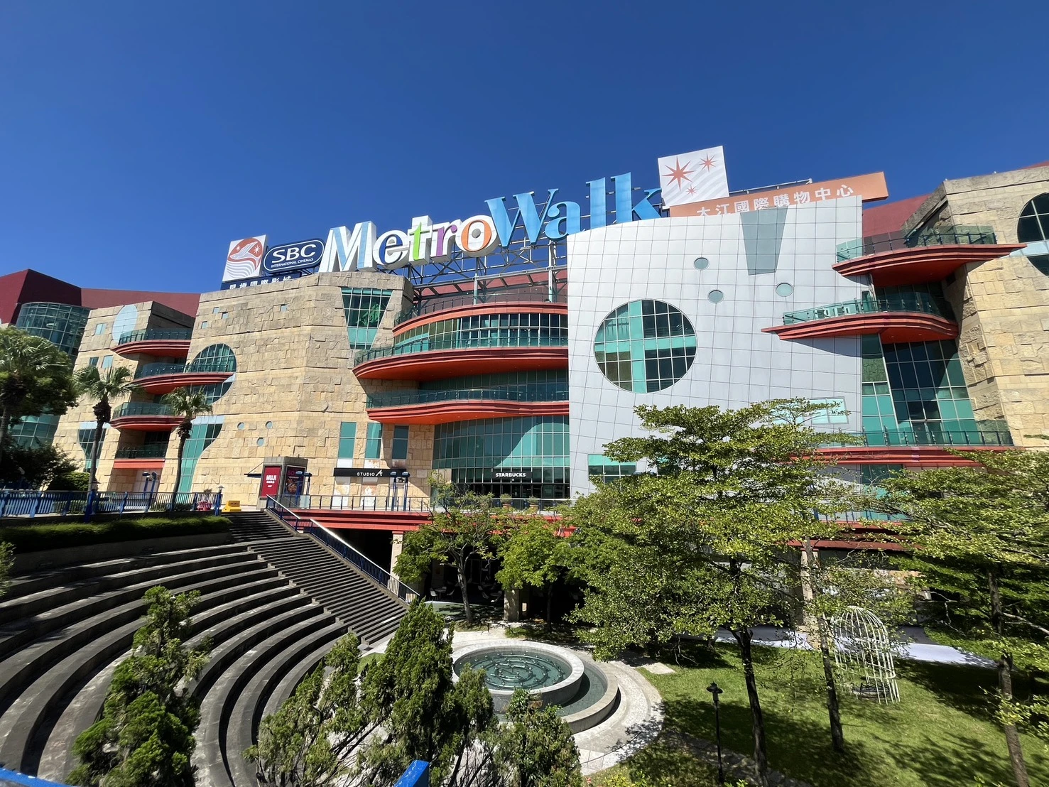 桃園大江購物中心建築外觀，晴朗藍天下的多層樓商場與戶外廣場。