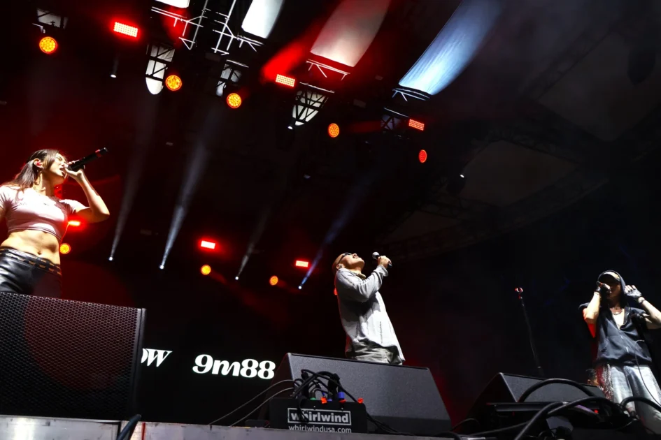 ØZI、YELLOW黃宣與9m88三位歌手在舞台上持麥克風演唱，背後有燈光與螢幕背景。