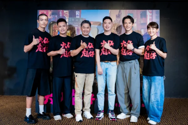 六位男女演員與導演站成一排，在電影背板前對鏡頭微笑並比讚。