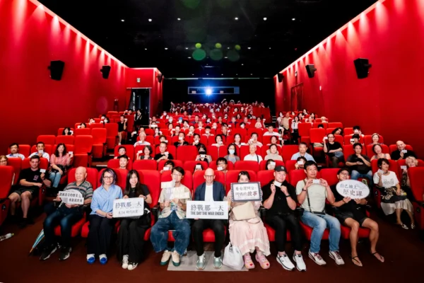 紀錄片《終戰那一天》首映會現場，導演、與談人與全場觀眾在紅幕影廳內舉著紀念票卡合影。