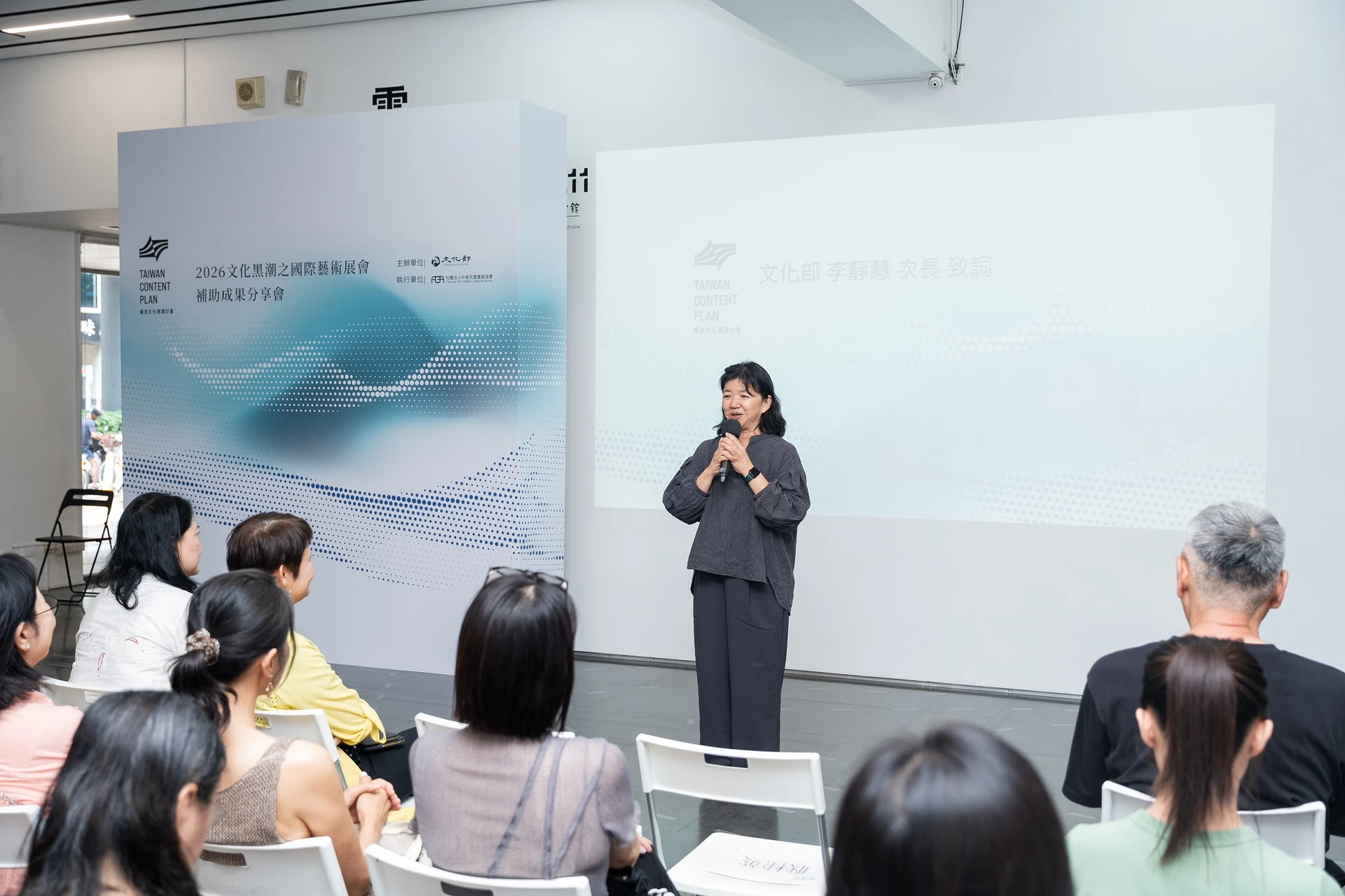 文化部政務次長李靜慧於台前持麥克風發言,背後投影幕顯示活動標題。