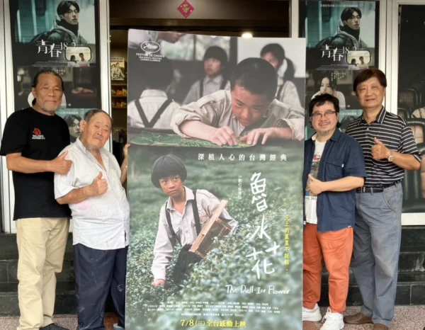 四名男子站在戲院門口，中間有人手持《魯冰花》電影宣傳海報，兩側人員比讚。