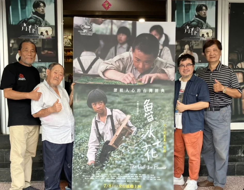 四名男子站在戲院門口，中間有人手持《魯冰花》電影宣傳海報，兩側人員比讚。