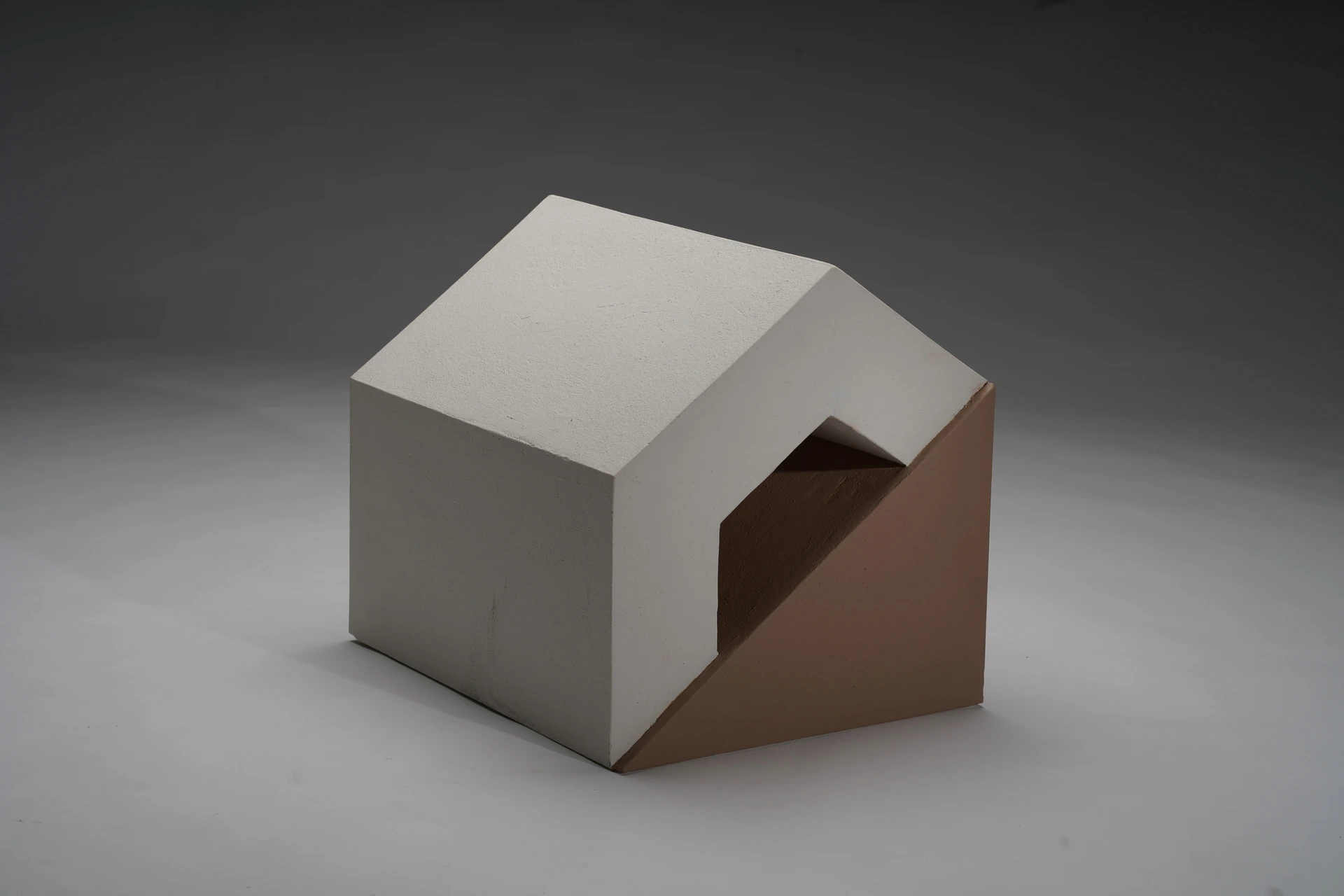幾何造型的陶塑作品,外型如房屋結構,白色屋頂造型結合下方淺棕色斜面基座。