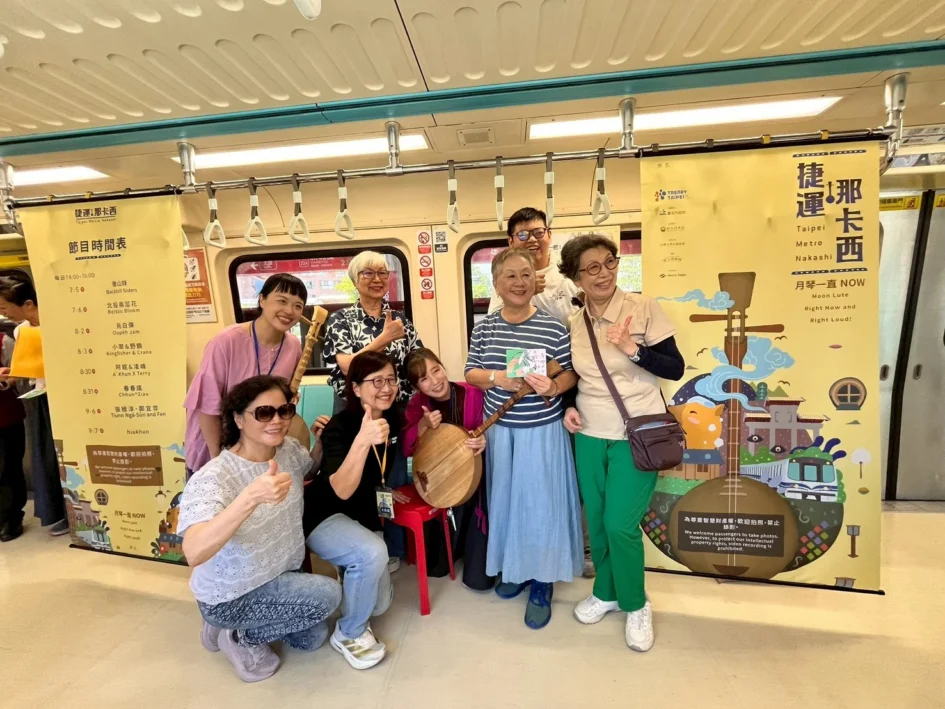 多位民眾與演出者在捷運車廂內開心比讚合影，車廂內貼有「捷運那卡西」活動海報與節目時間表。
