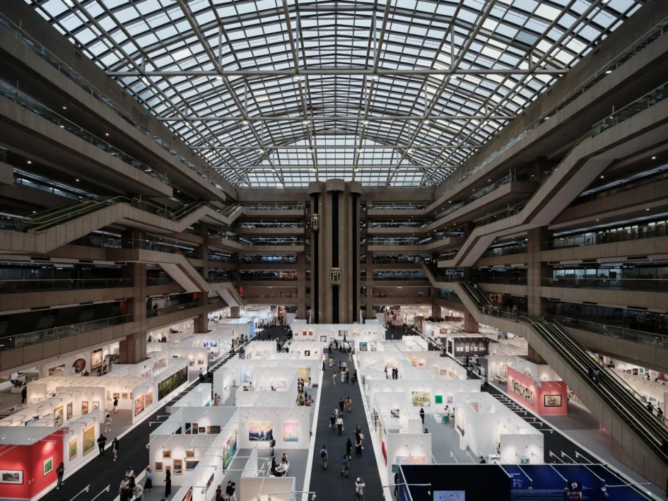 台北世貿一館展場內部的高空俯瞰視角，白色展位整齊排列，通道上可見觀展人潮與挑高氣派的建築結構。