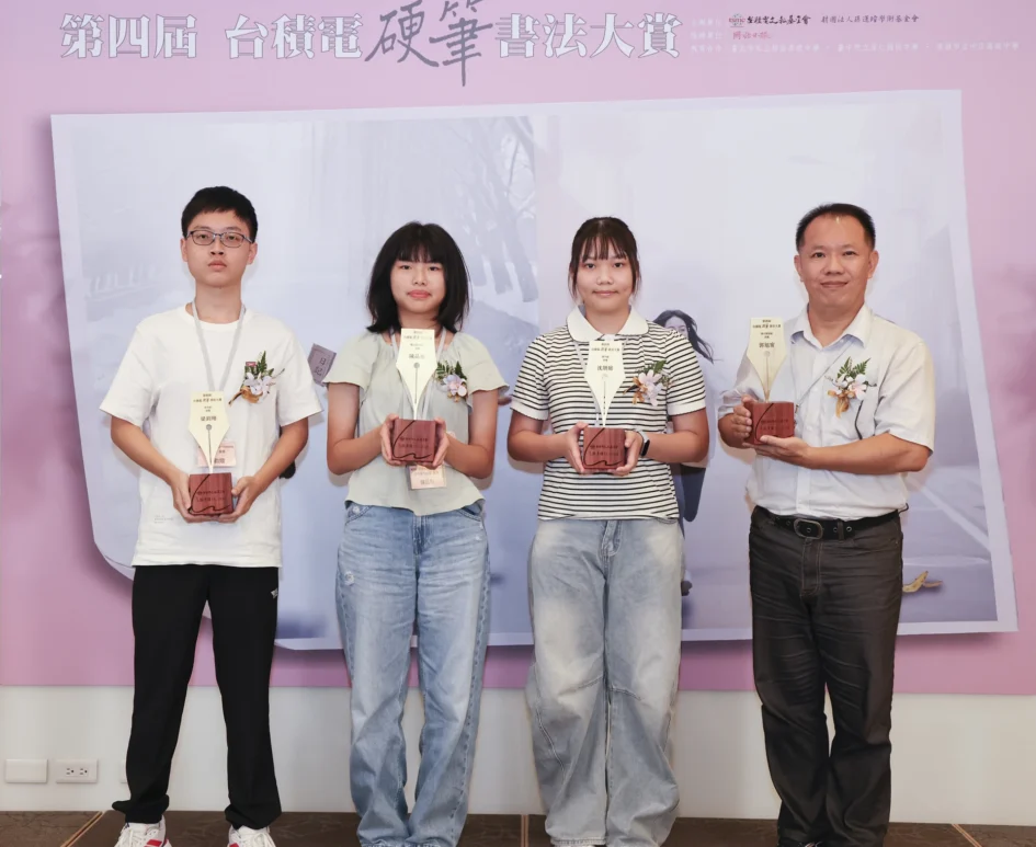 四位首獎得獎者站在背板前合影，由左至右分別為高中組梁鈞翔、國小高年級組陳品彤、國中組沈妍庭、國小教師組郭旭甯老師，四人手中皆捧著木製獎座。
