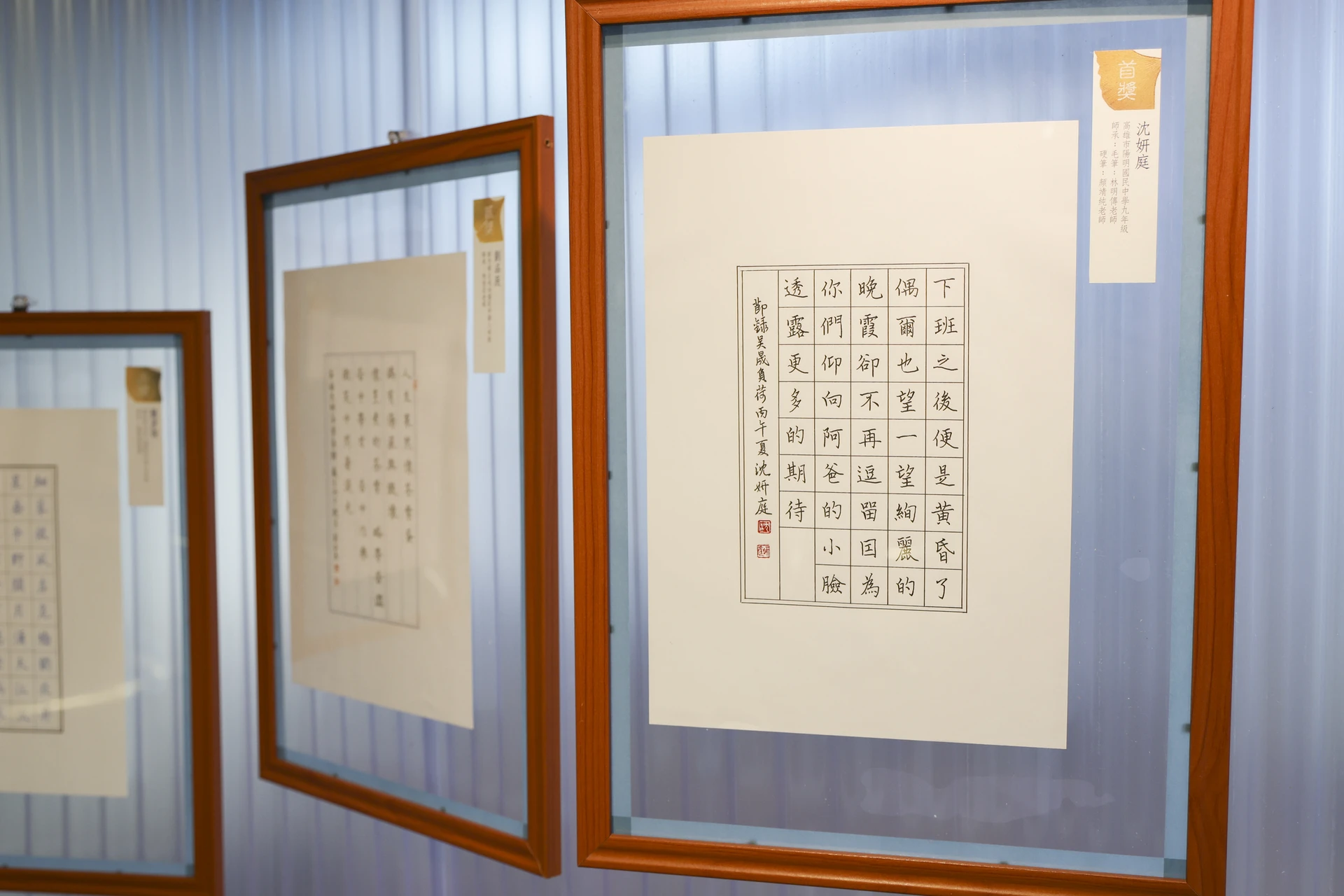 裱框展示的硬筆書法作品,白色方格紙上以細緻筆畫書寫工整漢字,右上方貼有金色首獎標籤,標註作者為沈妍庭。