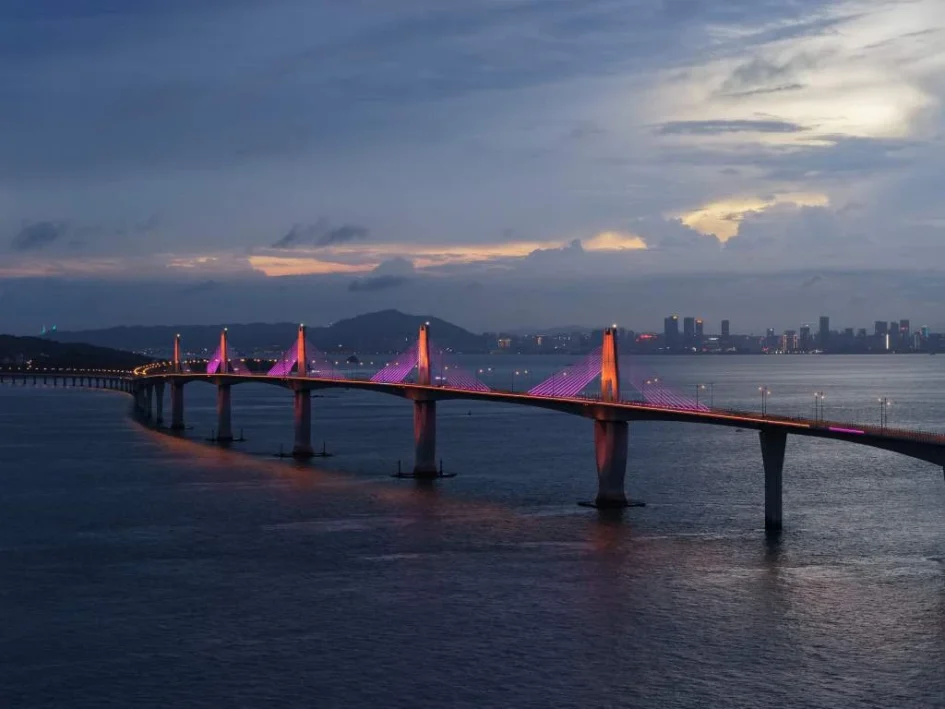 黃昏與夜色交織下點綴紫色燈光的金門大橋橫跨海面，遠處可見城市燈火
